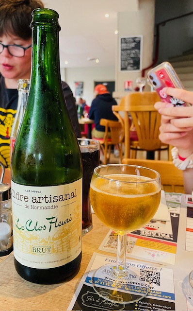 A traditional green bottle of Normandy cidre next to a glass full with cidre. 