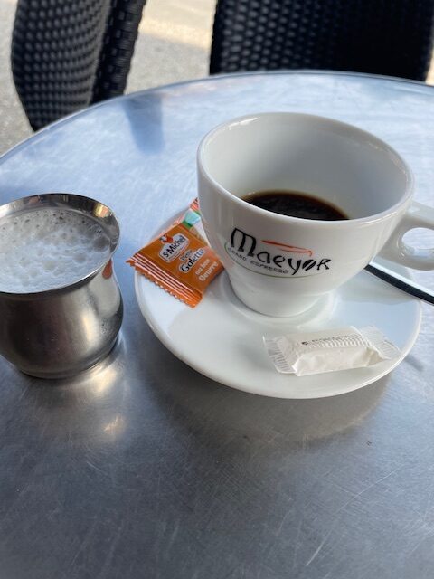 A cup of espresso coffee with a jug of hot milk to make a cafe au lait.